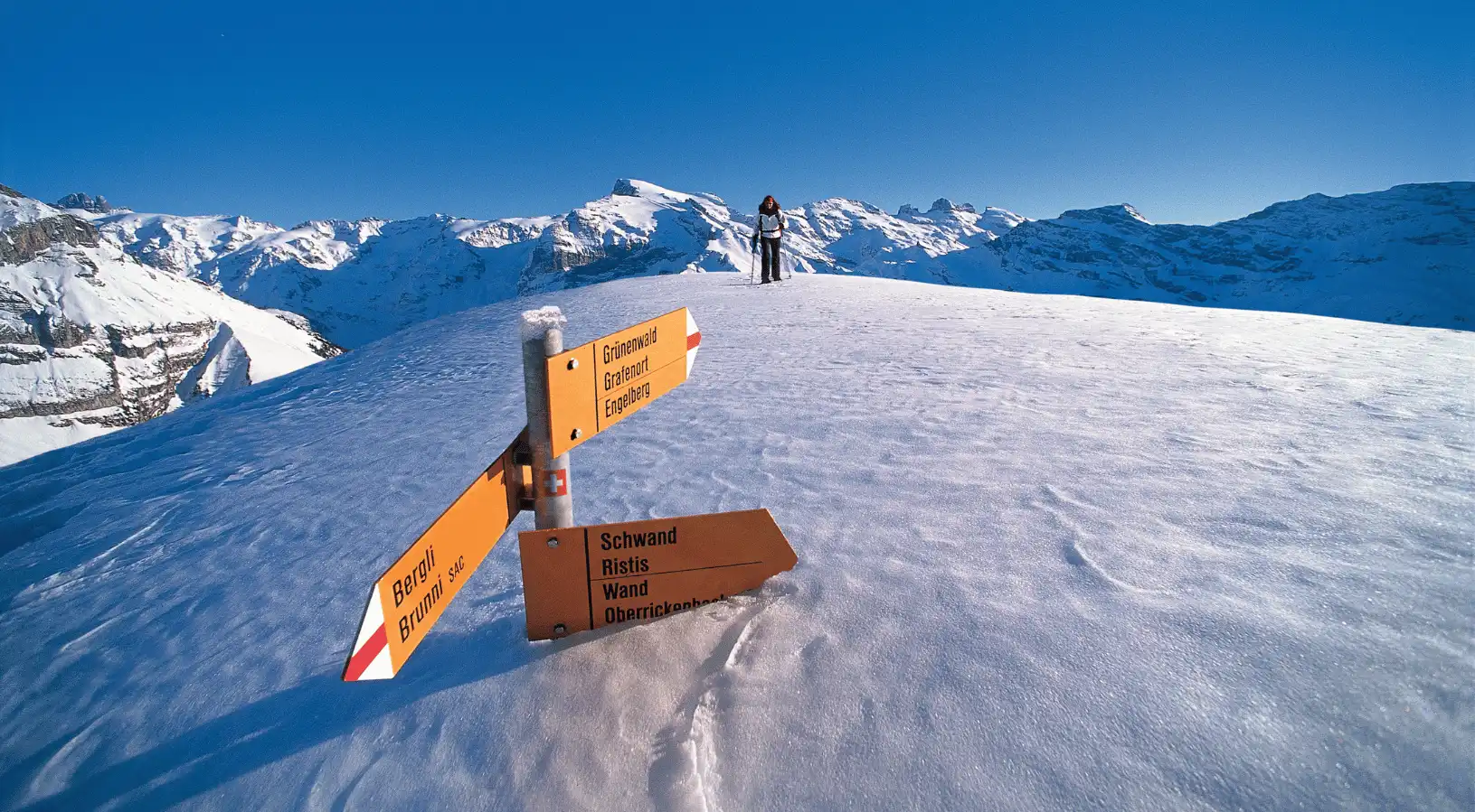 Snow-covered hiking trail signpost in the Swiss Alps with panoramic mountain views, showcasing scenic routes accessible via the Best place to buy the Swiss Travel Pass.