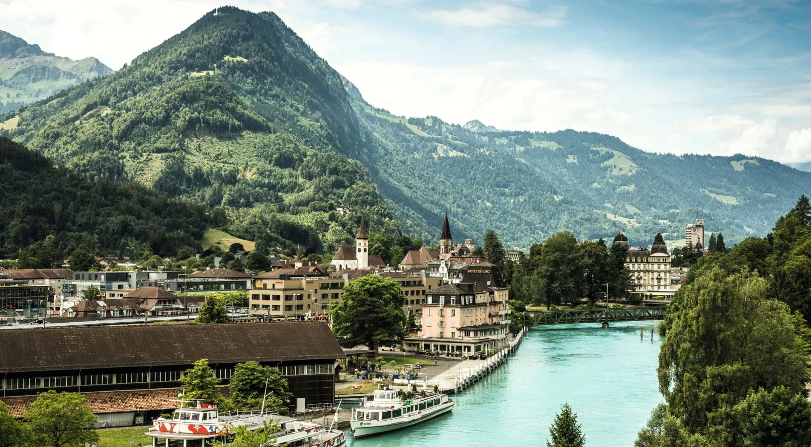 Panoramic view of Interlaken with alpine peaks, turquoise rivers, and charming village architecture, a highlight destination in Switzerland honeymoon packages.