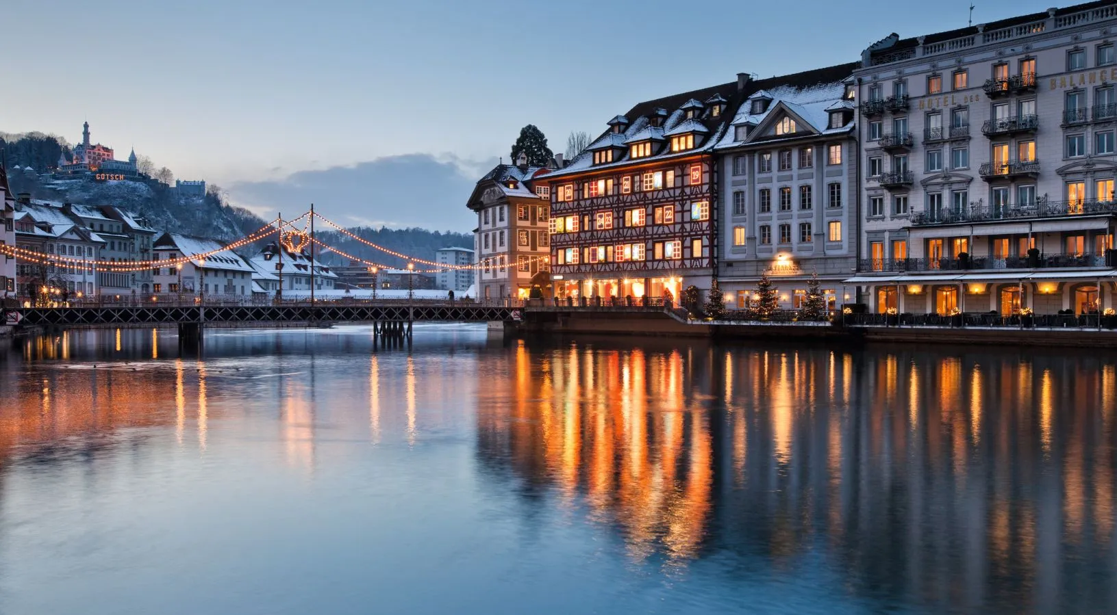 Illuminated waterfront buildings and the Reuss River in Lucerne at dusk, showcasing the romantic atmosphere ideal for Switzerland honeymoon packages.