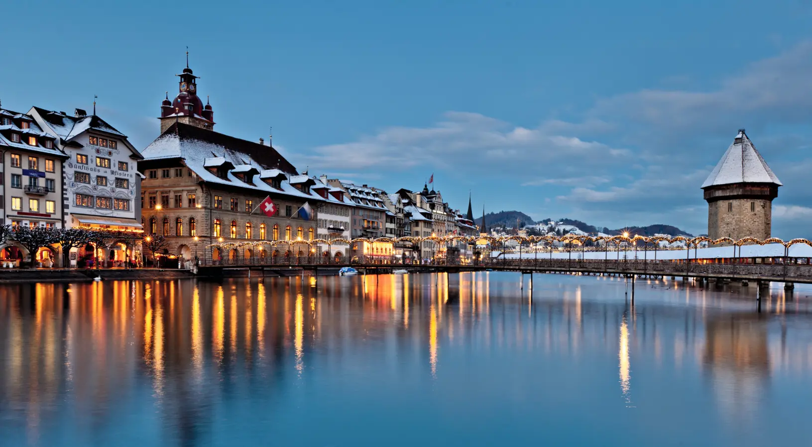 Illuminated waterfront buildings and the Reuss River in Lucerne at dusk, showcasing the romantic atmosphere ideal for Switzerland honeymoon packages.