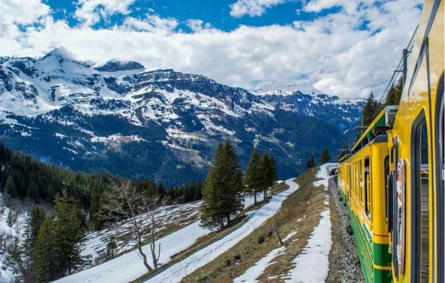 A train traveling through snow-covered mountainous terrain in winter, surrounded by majestic peaks and frosty landscapes.