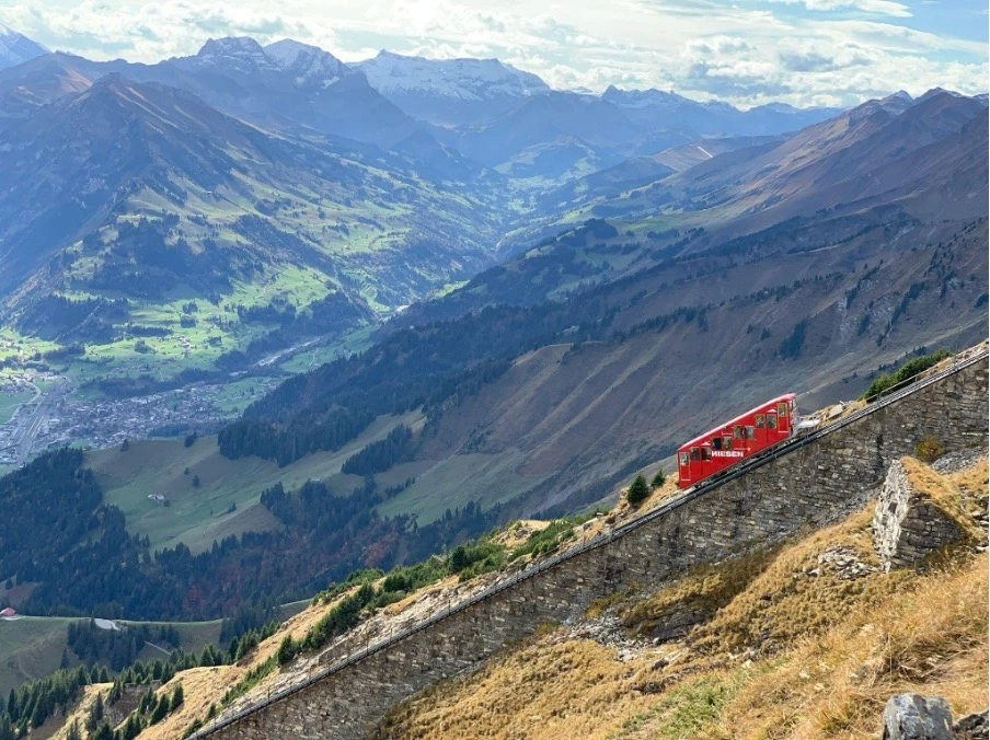 A view of the Niesen Funicular staircase, a steep set of steps leading up the mountain, with breathtaking panoramic views of the surrounding Swiss Alps and Lake Thun below.